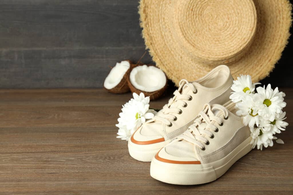 Une paire de baskets éthiques avec une fleur, des cocos et un chapeau en paille posés sur une surface en bois.