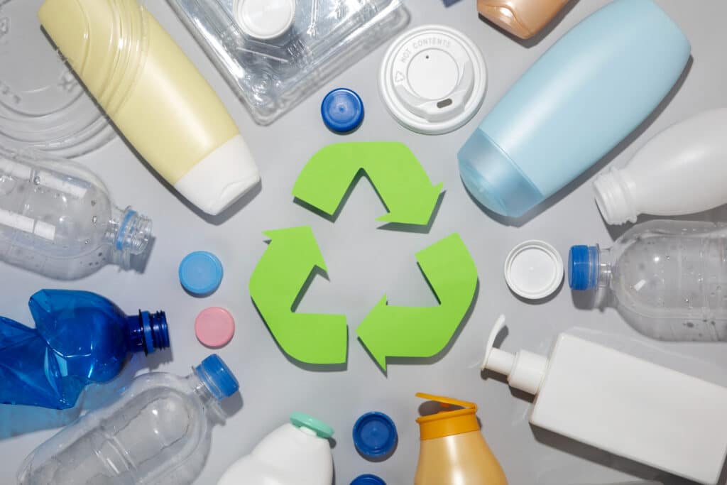 Des boîtes de shampoing et de produits en plastique ainsi que des bouteilles en plastique entourent le sigle de recyclage de couleur vert.