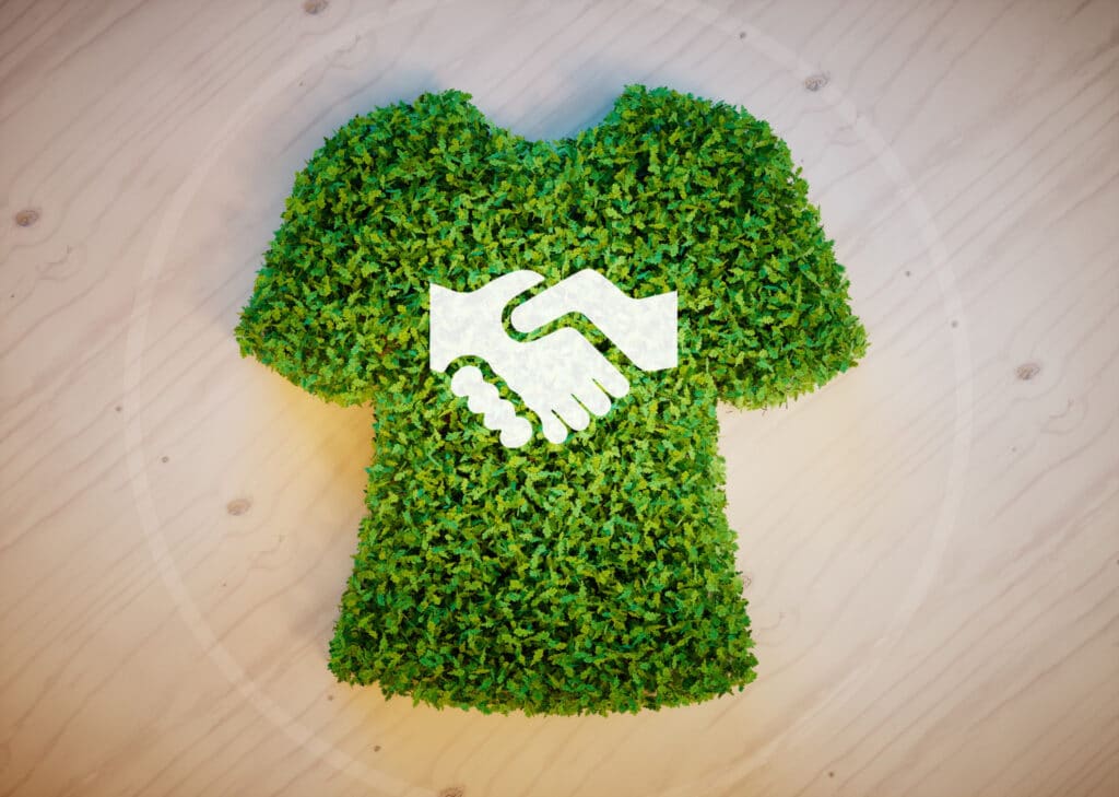 Un T-shirt fait de feuilles vertes. Sur le devant du T-shirt se trouvent une image de deux mains de couleur blanc se serrant.