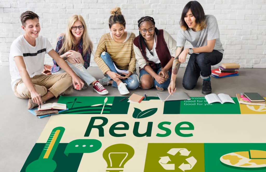 Des jeunes: un garçon et 4 filles, assis devant un tapis où est inscrit le mot "Reuse" avec différents croquis de couleur vert exprimant le concept d'éco-responsabilité.